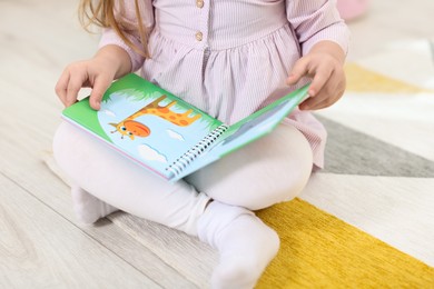 Photo of Little girl with book on floor in kindergarten, closeup
