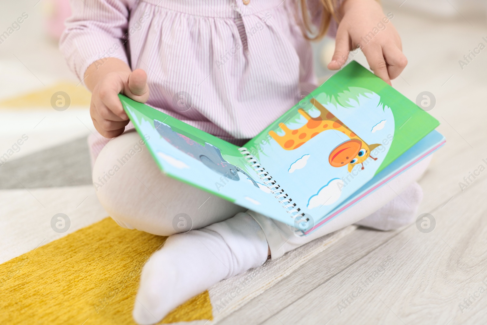 Photo of Little girl with book on floor in kindergarten, closeup