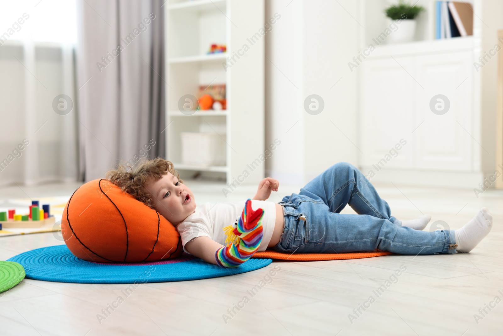 Photo of Cute little boy playing with funny sock puppet on floor in kindergarten