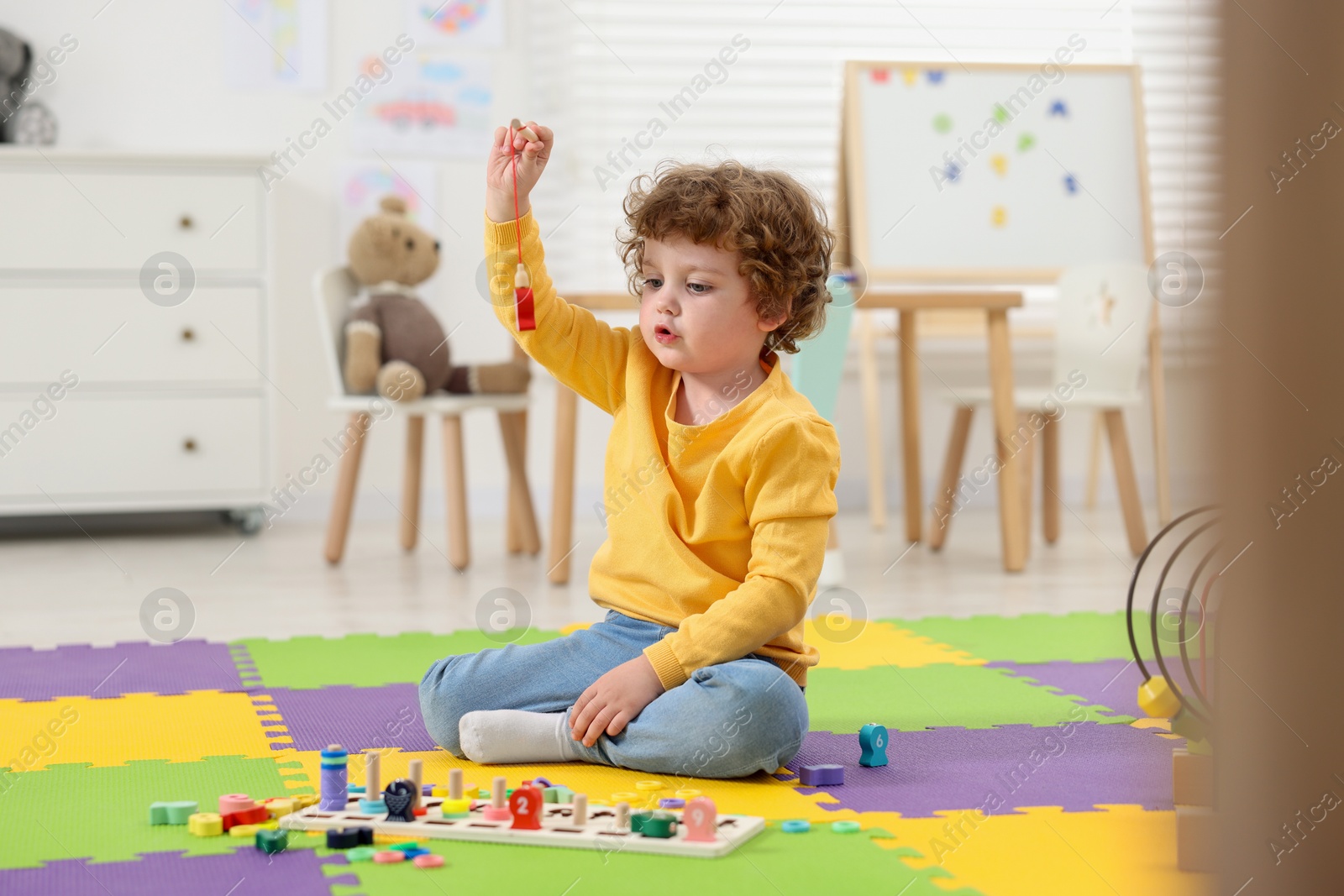 Photo of Cute little boy playing with math game Fishing for Numbers on puzzle mat in kindergarten