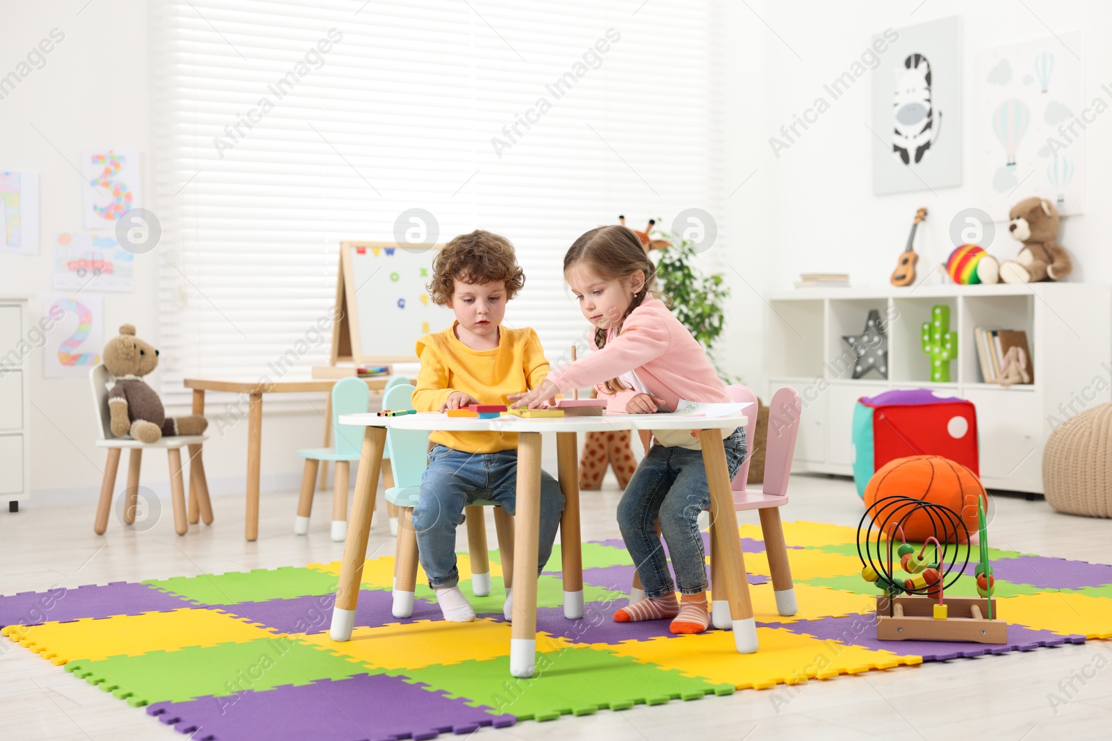 Photo of Cute little children playing with colorful toy pyramid at white table in kindergarten