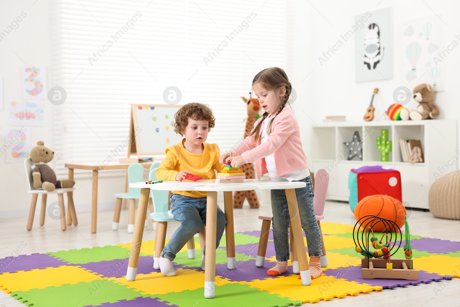 Photo of Cute little children playing with colorful toy pyramid at white table in kindergarten