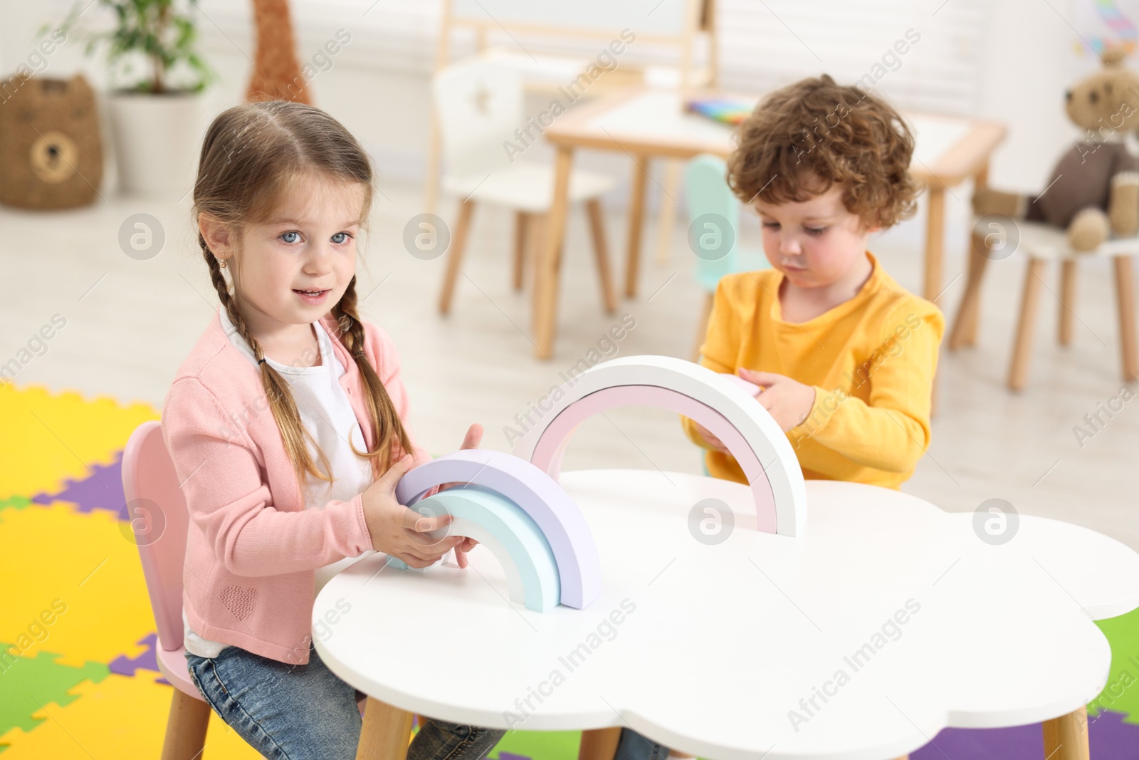 Photo of Cute little children playing with colorful toy rainbow at white table in kindergarten