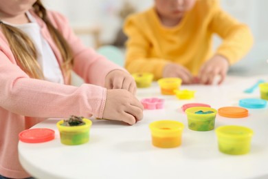 Photo of Little children modeling from plasticine at white table in kindergarten, closeup