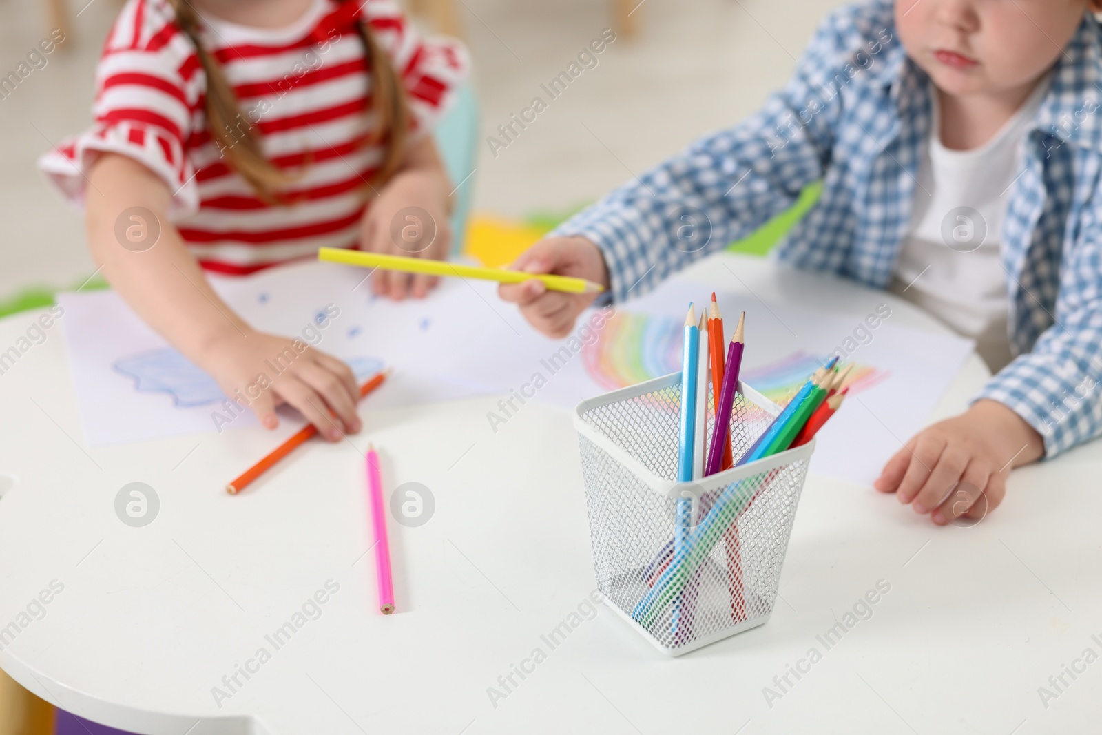 Photo of Little children drawing with colorful pencils at white table in kindergarten, selective focus