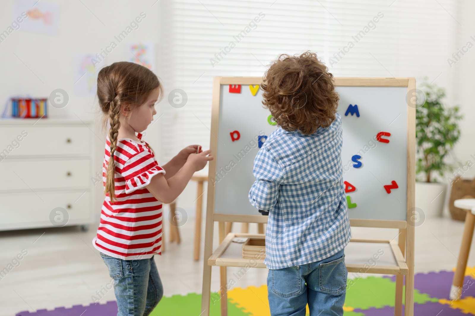 Photo of Cute little children learning alphabet with magnetic letters on board in kindergarten