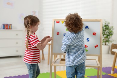 Photo of Cute little children learning alphabet with magnetic letters on board in kindergarten