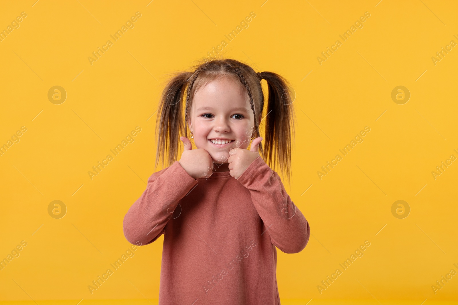 Photo of Cute little girl showing thumbs up on orange background