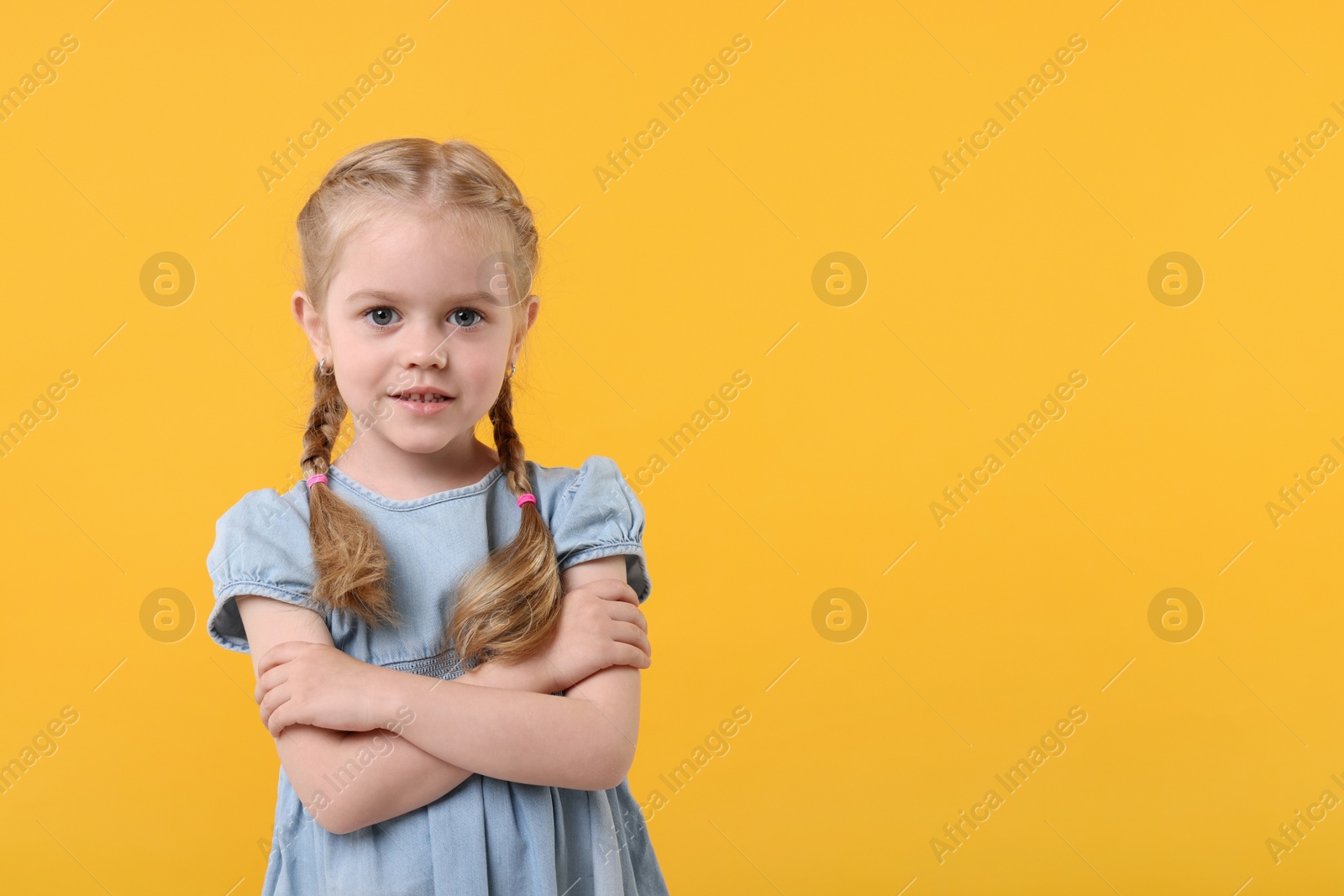 Photo of Portrait of cute little girl with crossed arms on orange background, space for text