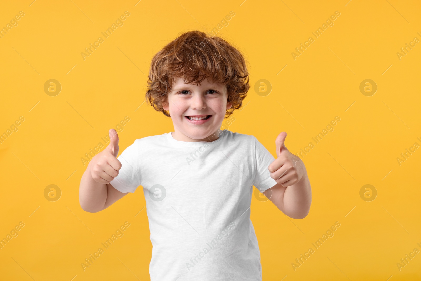 Photo of Cute little boy showing thumbs up on orange background