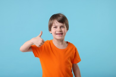 Photo of Cute little boy showing thumbs up on light blue background