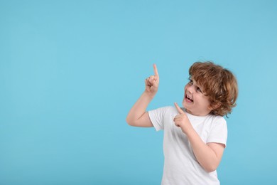 Cute little boy pointing at something on light blue background, space for text