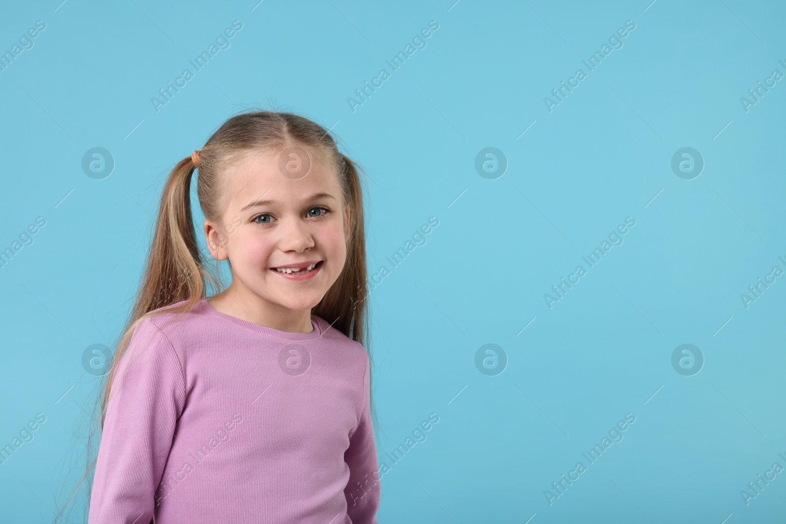 Photo of Portrait of cute little girl on light blue background, space for text