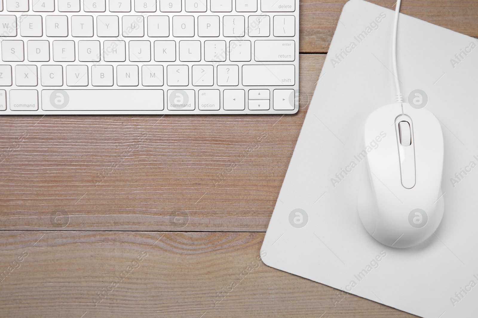 Photo of Wired mouse with mousepad and computer keyboard on wooden table, flat lay. Space for text