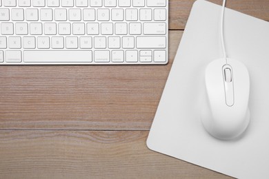 Photo of Wired mouse with mousepad and computer keyboard on wooden table, flat lay. Space for text