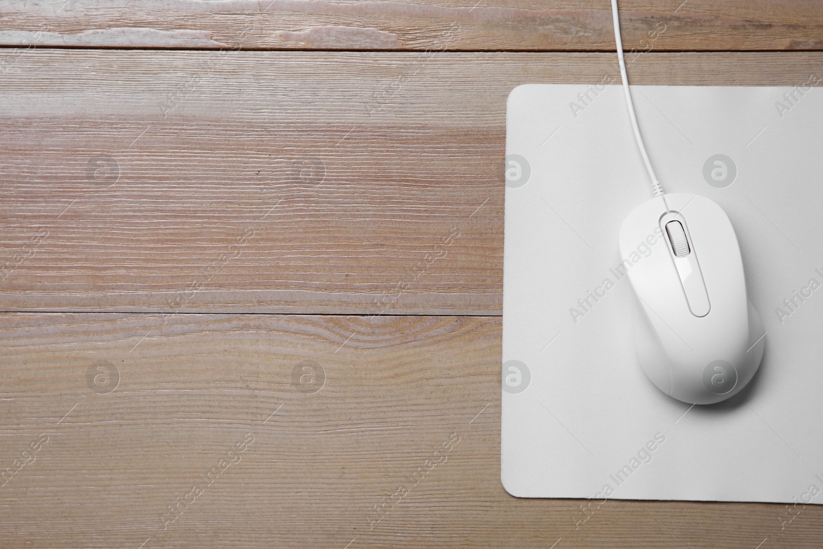 Photo of Wired mouse with mousepad on wooden table, top view. Space for text