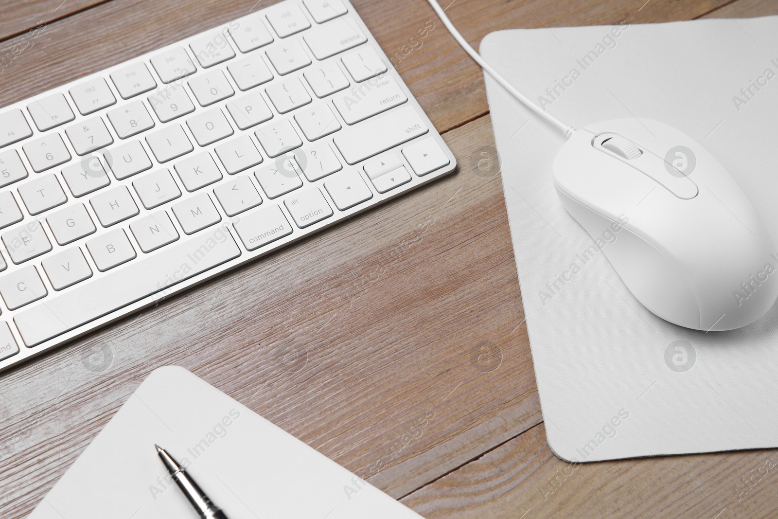 Photo of Wired mouse with mousepad, notebook, pen and computer keyboard on wooden table, above view