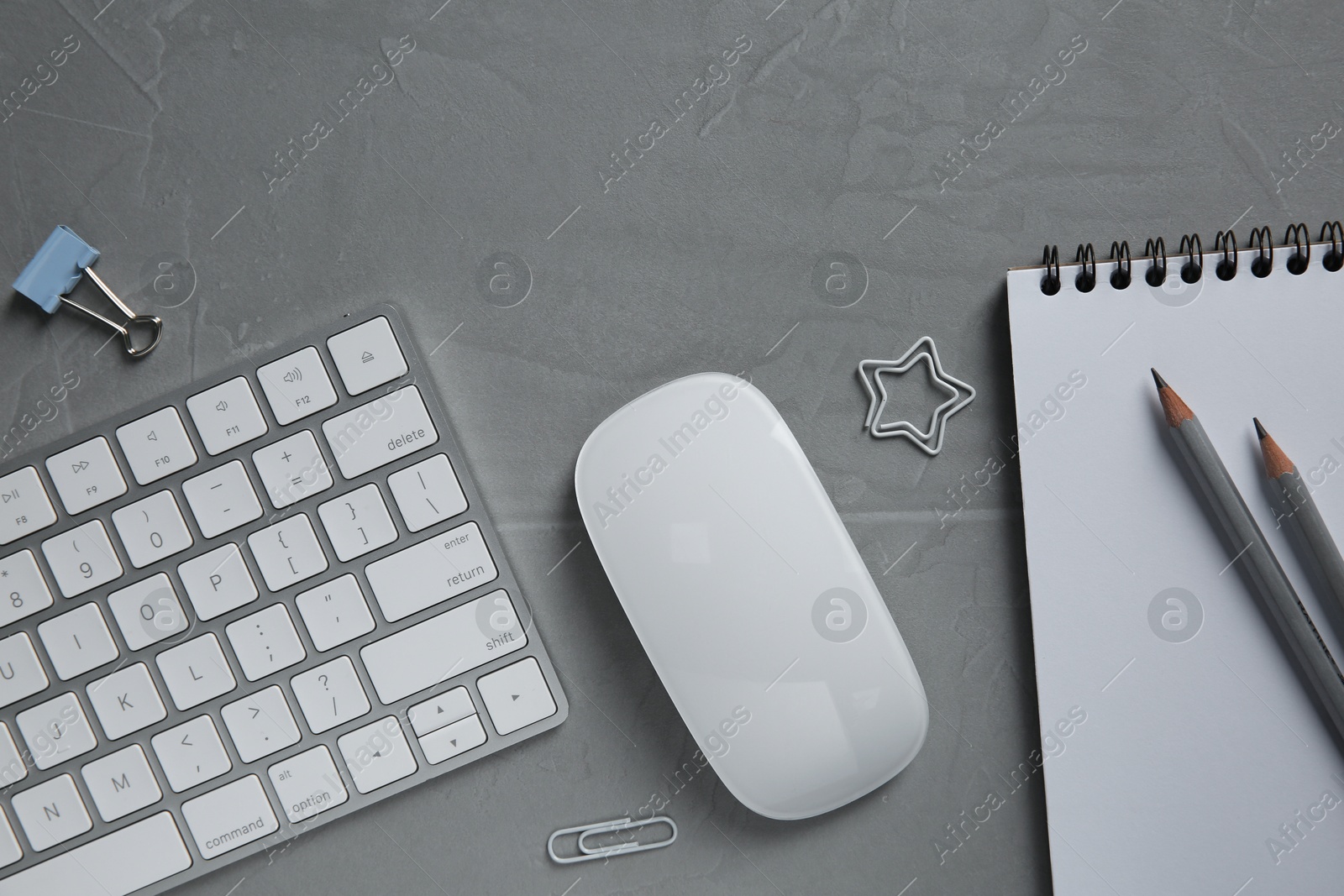 Photo of Wireless mouse, stationery and computer keyboard on grey textured table, flat lay