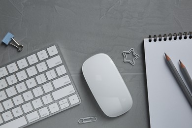 Wireless mouse, stationery and computer keyboard on grey textured table, flat lay