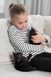 Photo of Little girl with cute fluffy kittens on sofa indoors