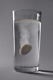 Effervescent pill dissolving in glass of water on grey background