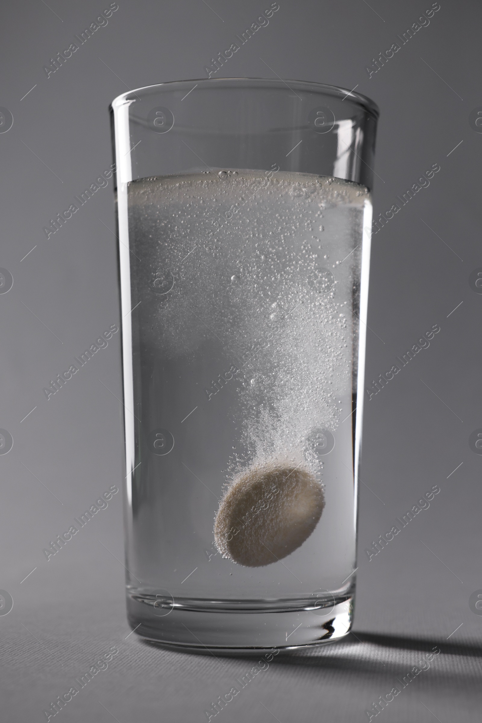Photo of Effervescent pill dissolving in glass of water on grey background