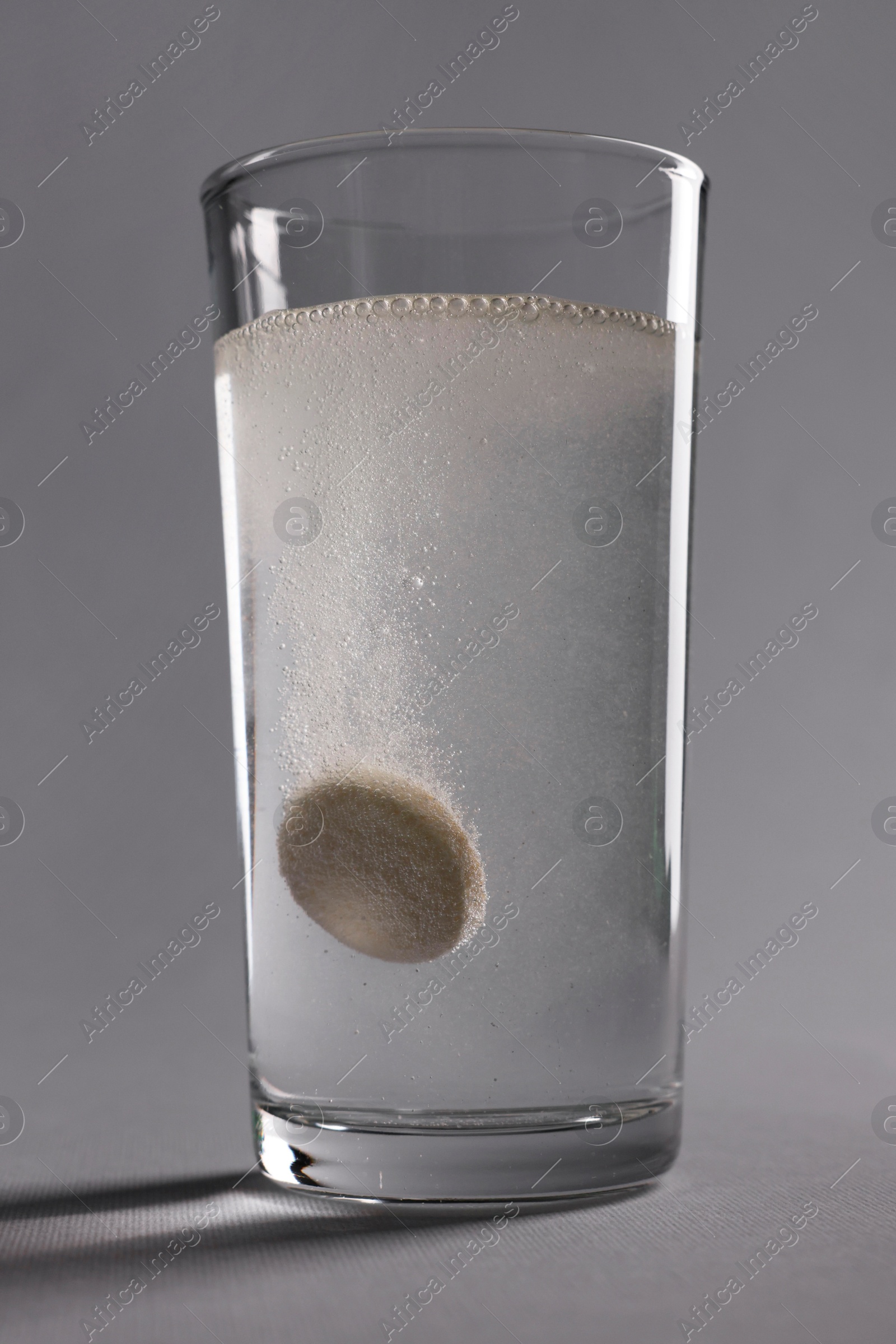 Photo of Effervescent pill dissolving in glass of water on grey background