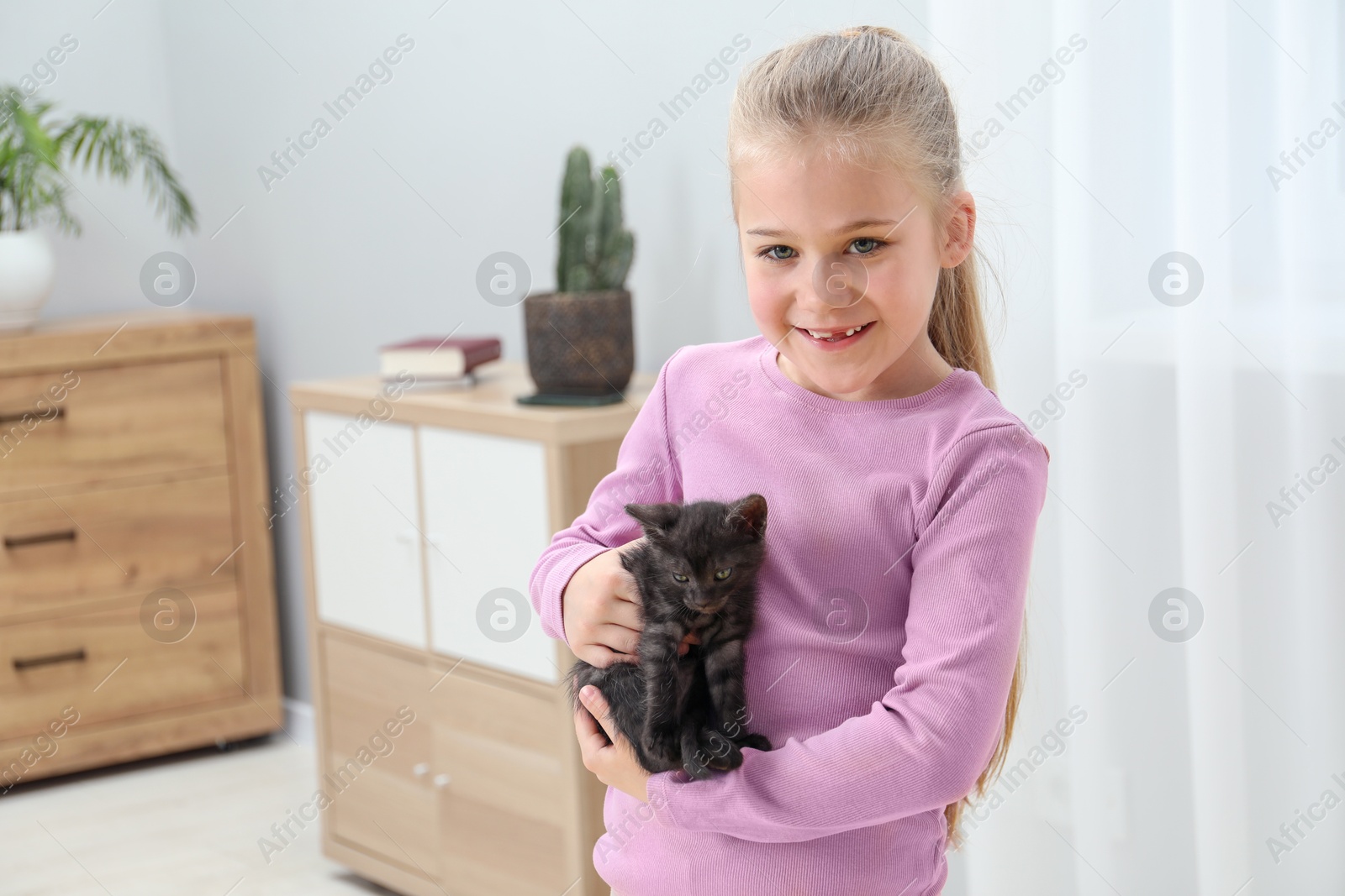 Photo of Little girl with cute fluffy kitten indoors, space for text