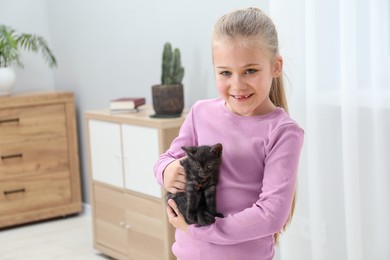 Little girl with cute fluffy kitten indoors, space for text