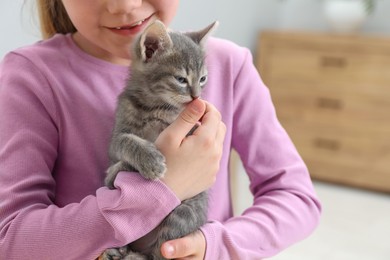 Photo of Little girl with cute fluffy kitten indoors, closeup
