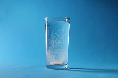 Photo of Effervescent pill dissolving in glass of water on light blue background