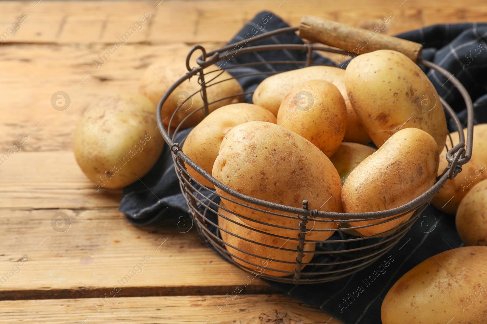 Photo of Many fresh potatoes in metal basket on wooden table, closeup