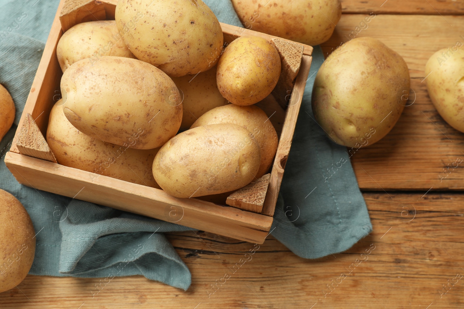 Photo of Many fresh potatoes in crate on wooden table, above view