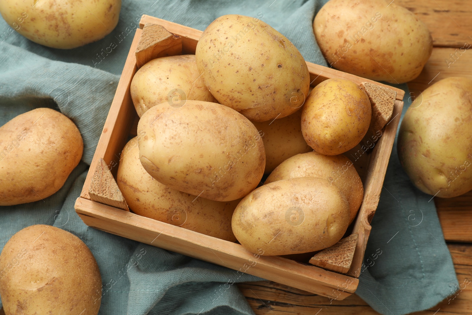 Photo of Many fresh potatoes in crate on wooden table, above view