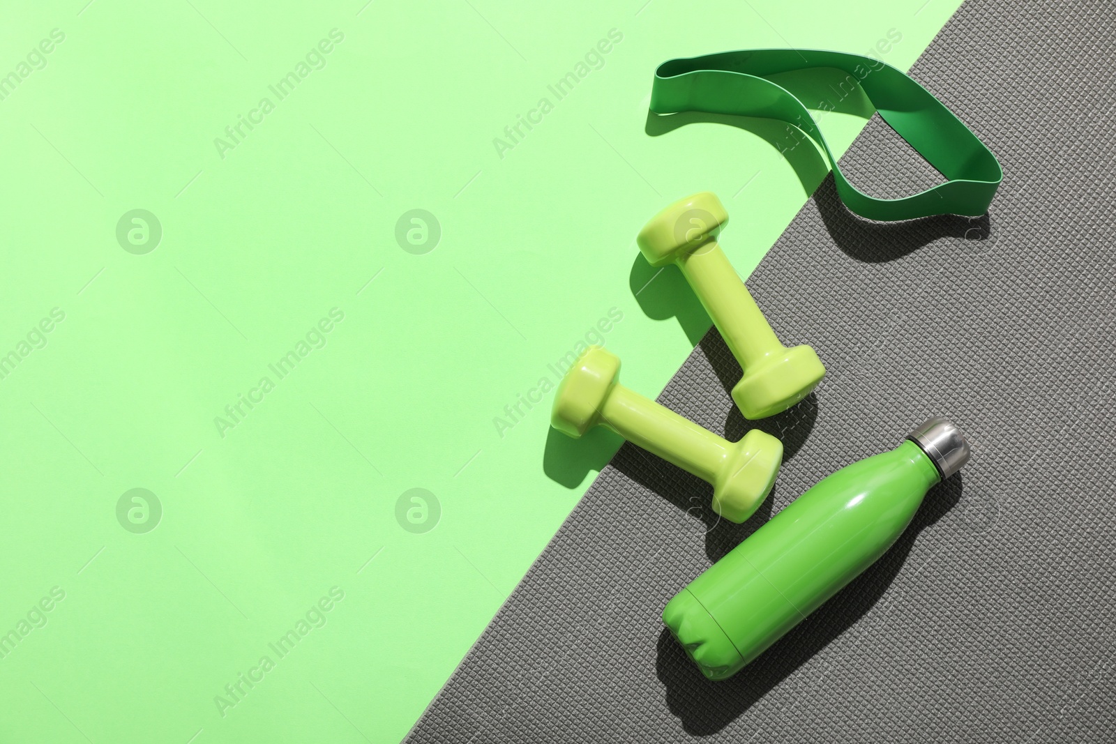Photo of Dumbbells, fitness elastic band, water bottle and mat on light green background, flat lay. Space for text