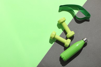 Dumbbells, fitness elastic band, water bottle and mat on light green background, flat lay. Space for text