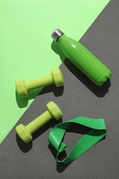 Dumbbells, fitness elastic band, water bottle and mat on light green background, flat lay