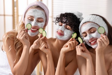 Photo of Happy friends with facial masks and cucumber slices in bathroom. Spa party