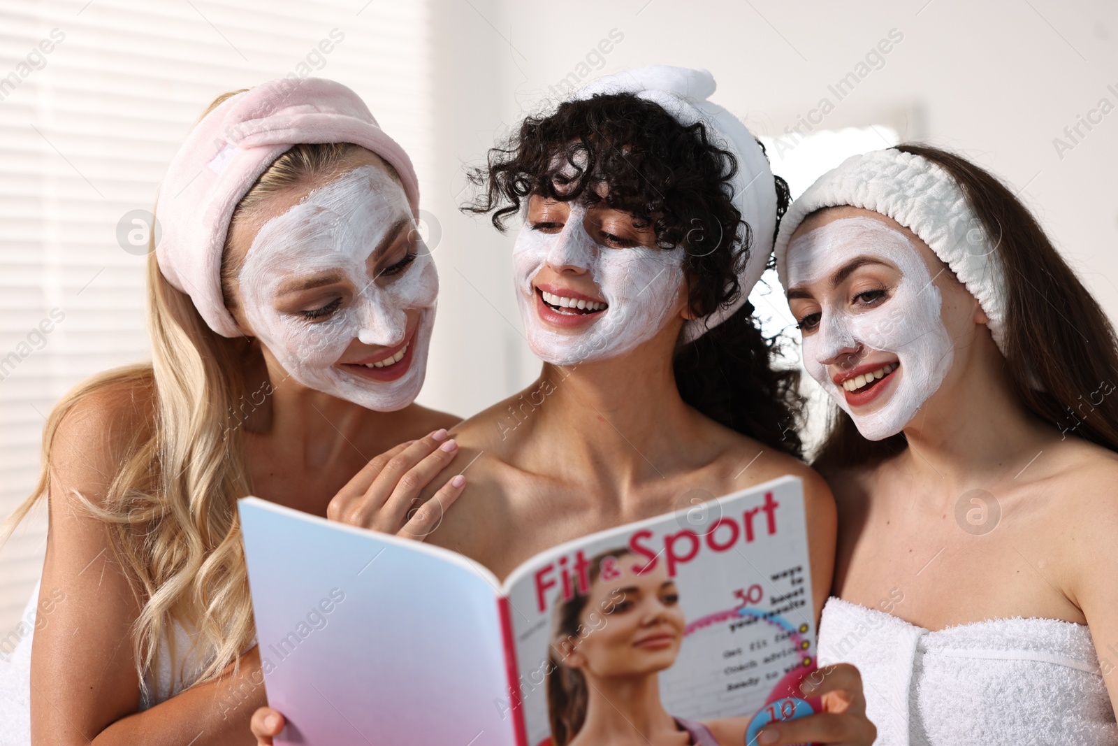 Photo of Happy friends with facial masks reading magazine in bathroom. Spa party