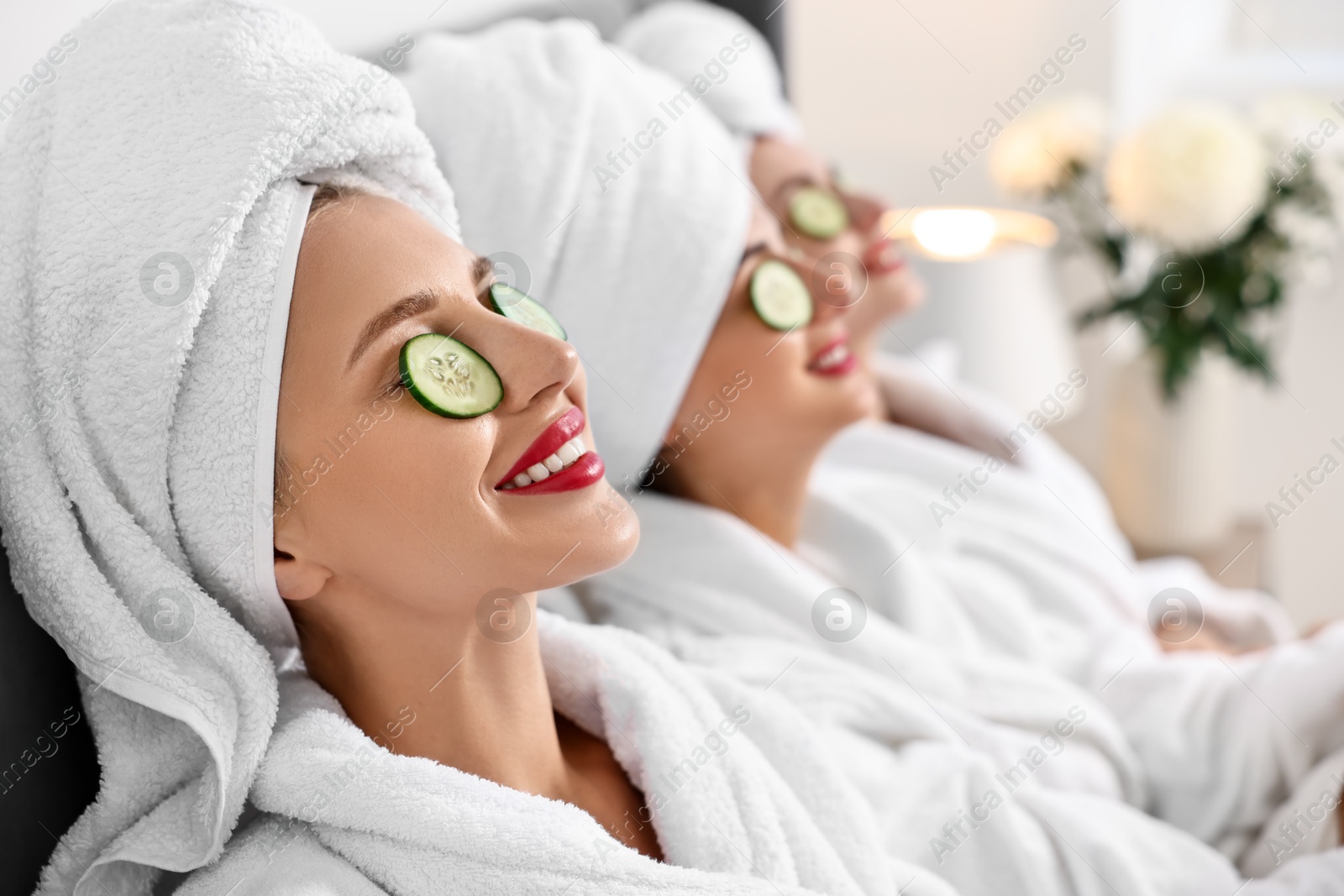 Photo of Happy friends in bathrobes with cucumber slices on bed, selective focus. Spa party