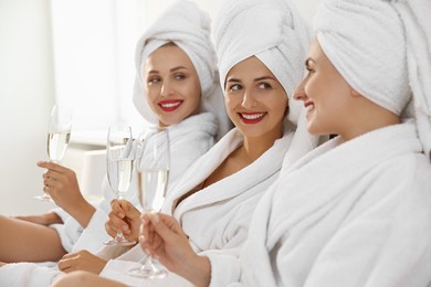 Happy friends in bathrobes with glasses of sparkling wine on bed, selective focus. Spa party