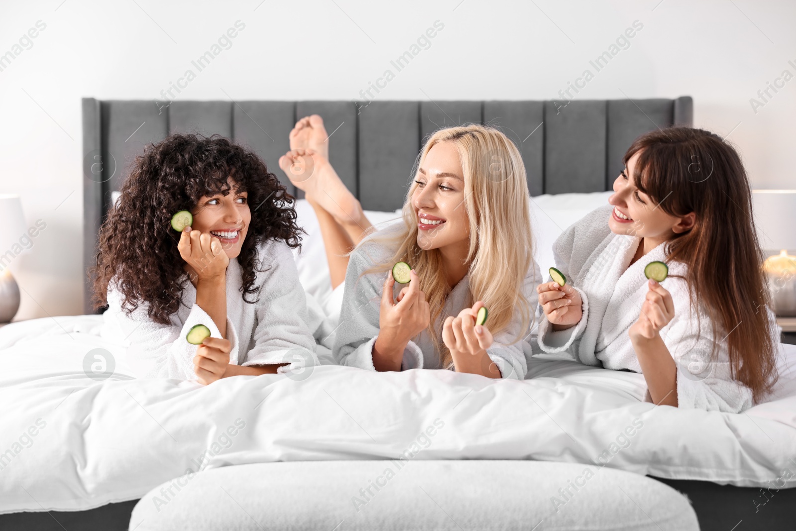 Photo of Happy friends with cucumber slices on bed. Spa party