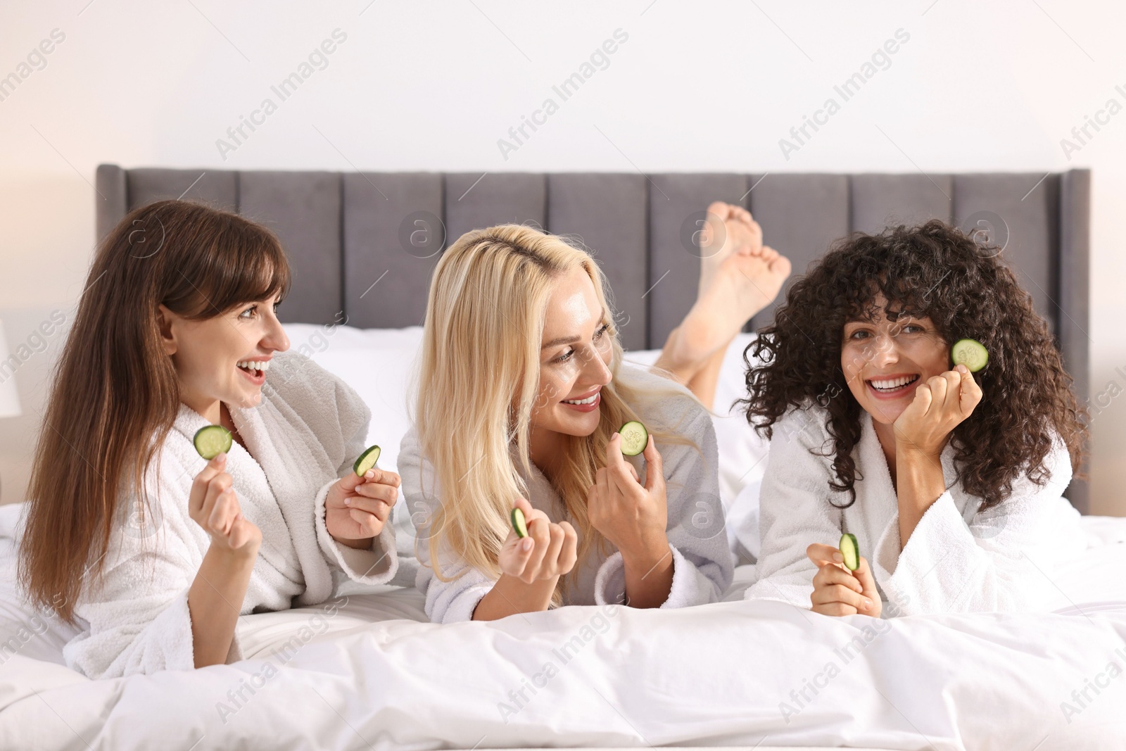 Photo of Happy friends with cucumber slices on bed. Spa party