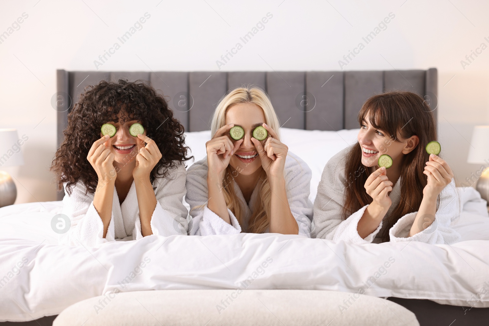 Photo of Happy friends with cucumber slices on bed. Spa party