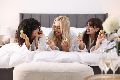 Photo of Happy friends with cucumber slices on bed. Spa party