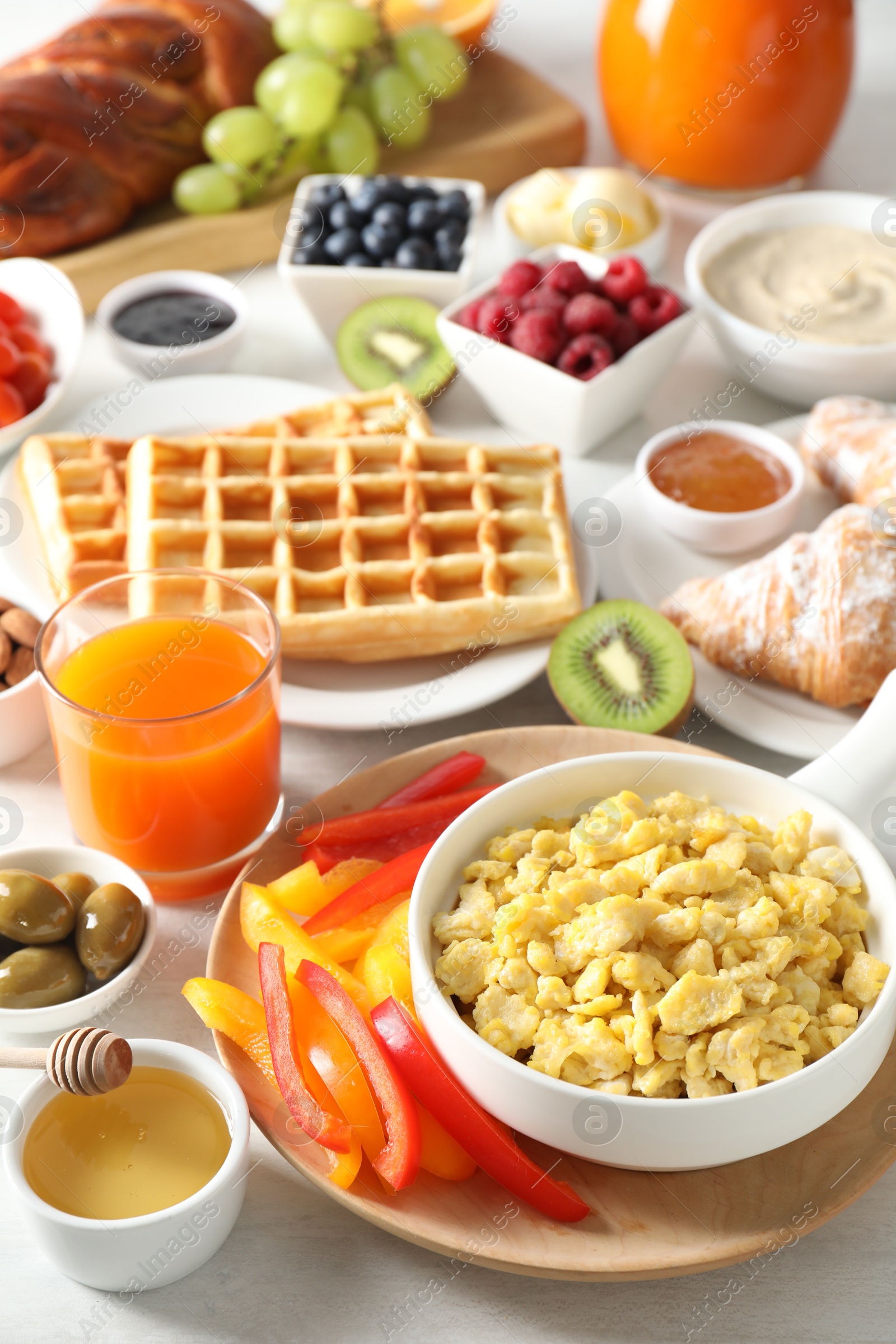 Photo of Tasty breakfast. Scrambled eggs in bowl, bell pepper, honey and other food on light table, closeup