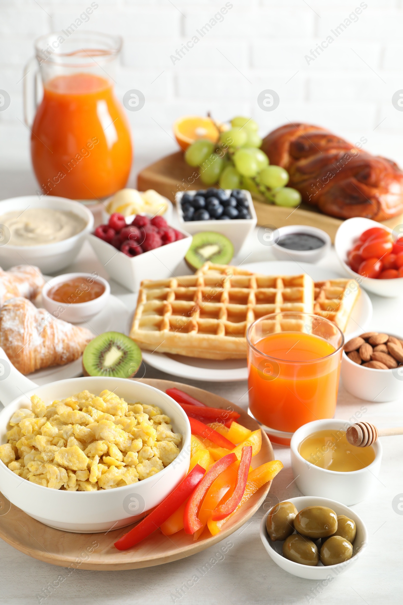 Photo of Tasty breakfast. Scrambled eggs in bowl, bell pepper, olives, honey and other food on light table