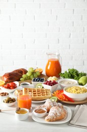 Photo of Tasty breakfast. Croissants, jam, honey and other food on light table against brick wall. Space for text