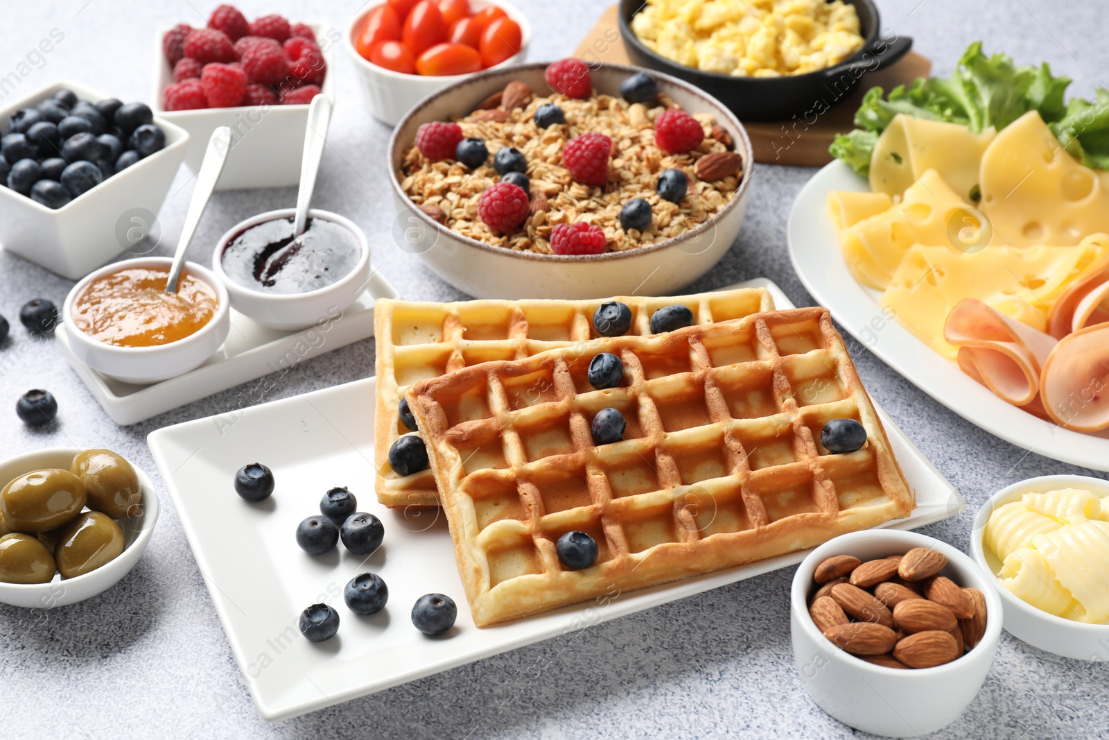 Photo of Tasty breakfast. Belgian waffles, blueberries and other food on grey textured table, closeup