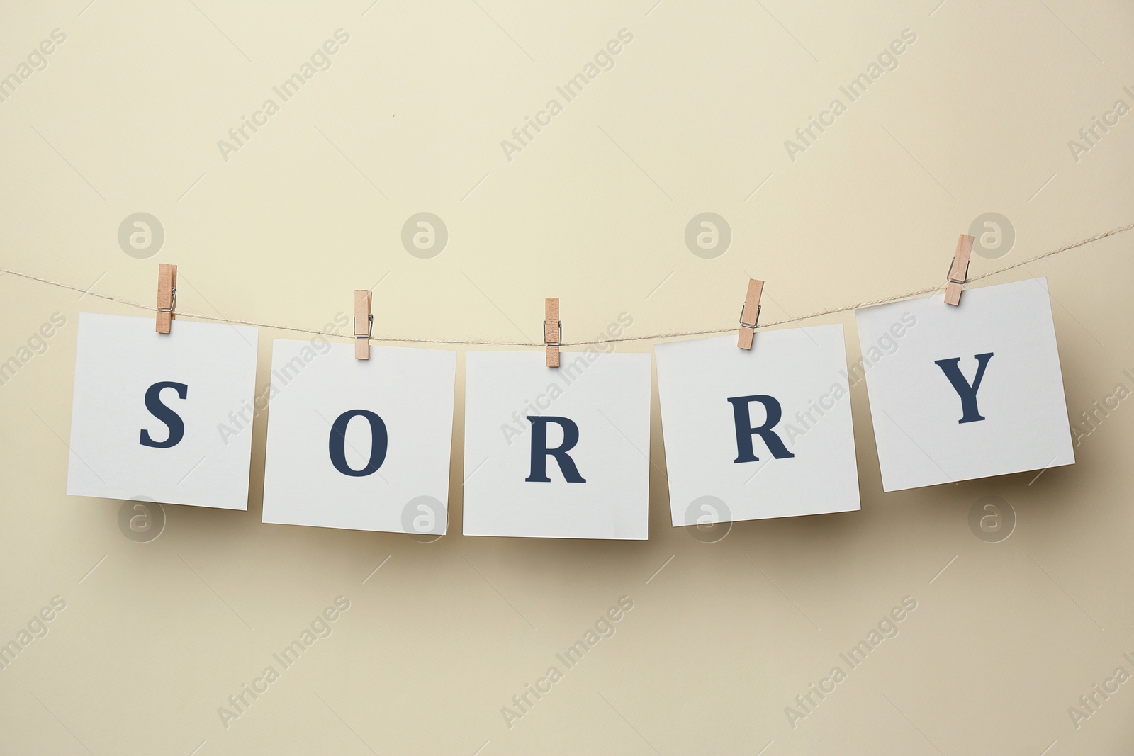 Image of Word Sorry made of paper notes with letters hanging on rope against beige background